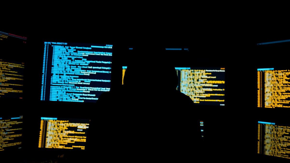 Silhueta de hacker em frente a telas com código